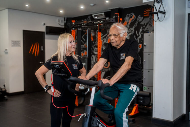 Trainer supporting older adult with cycling exercise for health and longevity