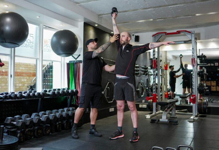 Trainer supporting client with overhead strength exercise as part of recovery training