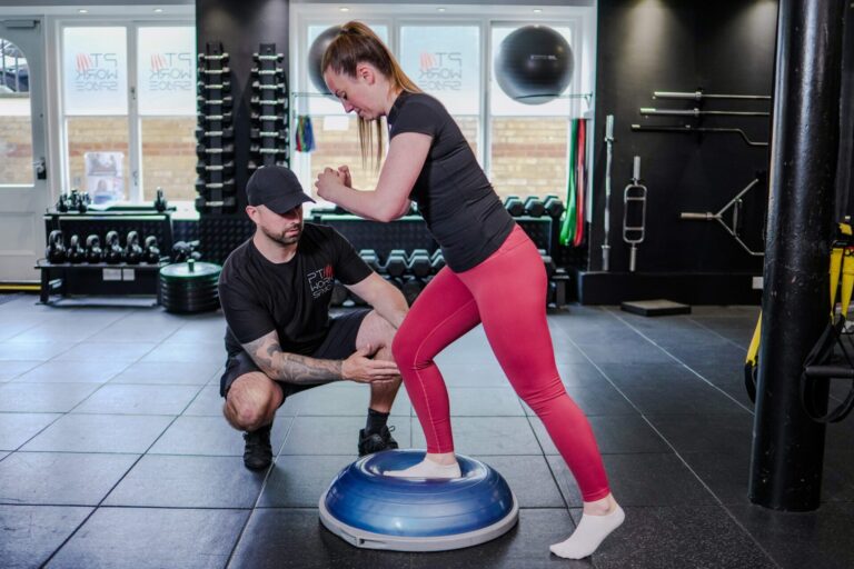Personal trainer supporting client with balance exercise during injury rehab session
