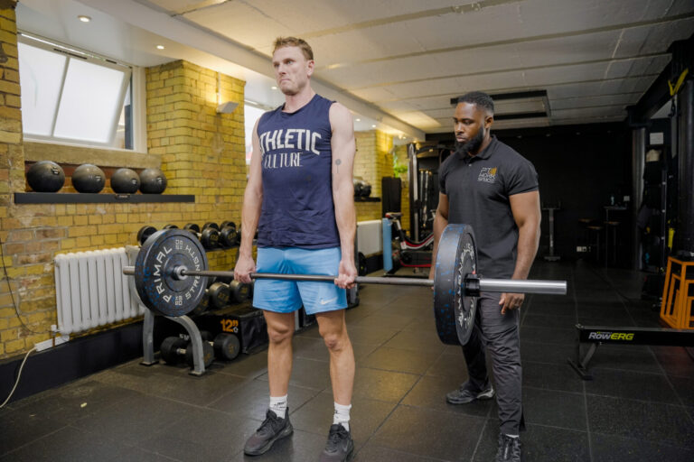 Male client performing barbell deadlift with trainer supervision – strength training and barbell technique in London.