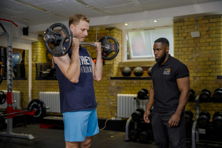 Male client lifting barbell under trainer supervision – men’s strength training session focused on muscle and power.
