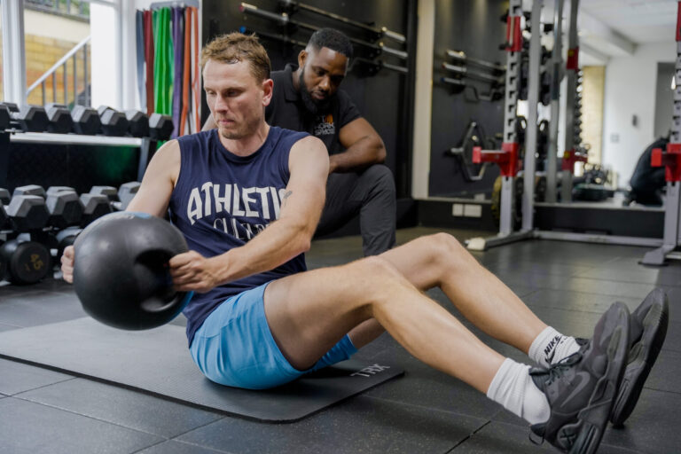 Client performing Russian twist with medicine ball under trainer supervision – core strength training and personal training support.