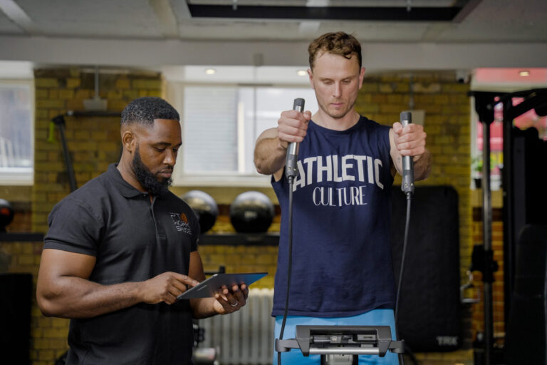 Trainer recording results while client performs fitness testing – personal training assessment for strength and progress tracking.
