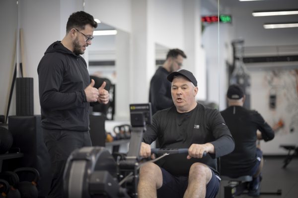 a man on a machine in a gym with personal trainer 