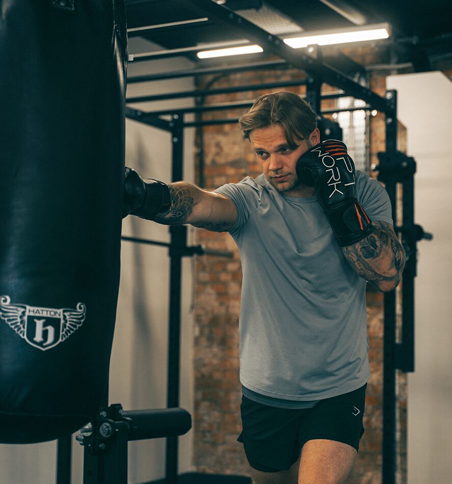 Client boxing with heavy bag during personal training session – power, conditioning and strength training.